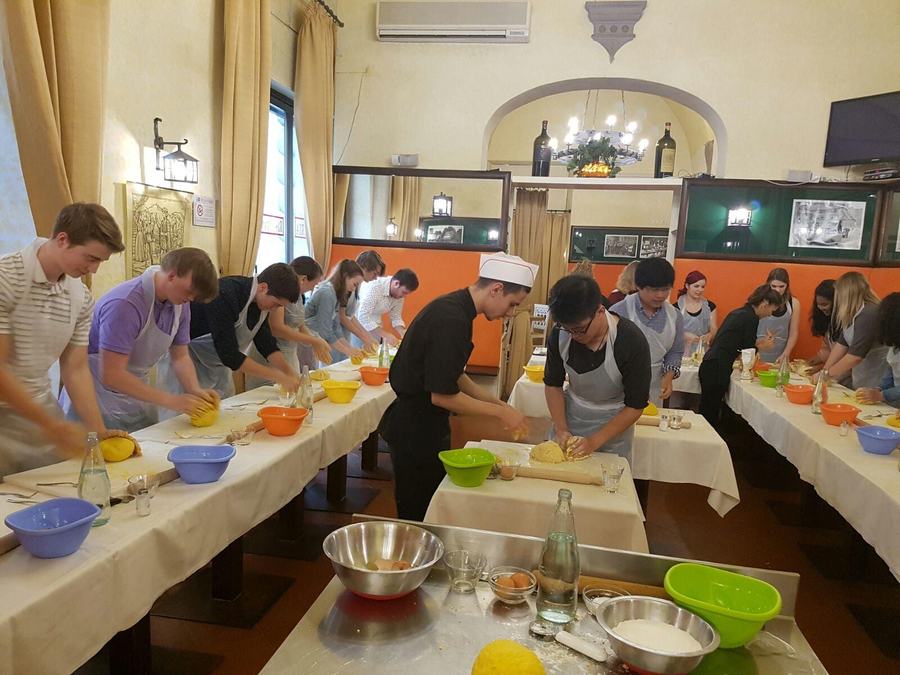 Gruppo di partecipanti alla cooking class impasta insieme allo chef nella sala allestita